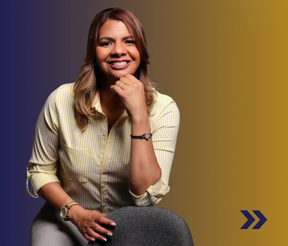 Carmen Núñez sonriendo, sentada, sobre fondo degradado azul y dorado